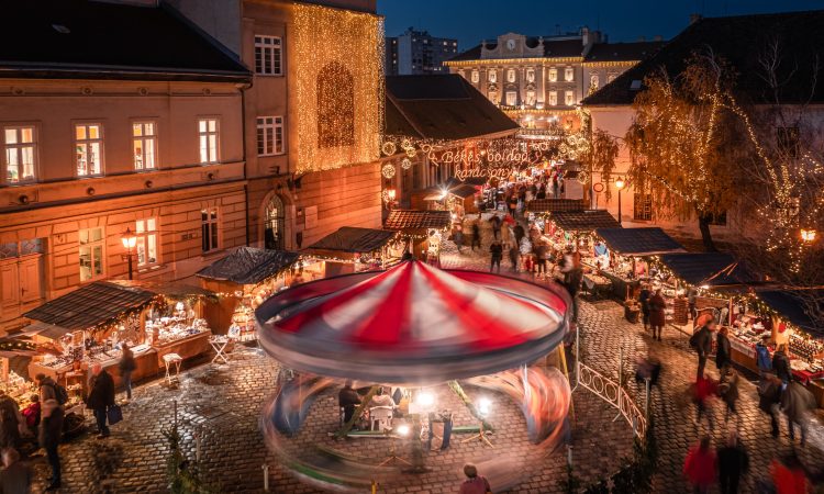 Budapest, Hungary - Aerial view of the Christmas market and carousel on Szentlelek square, Obuda at dusk. Decorative illuminated shops, festive decoration and Christmas signs on the streets of Buda with dark blue sky